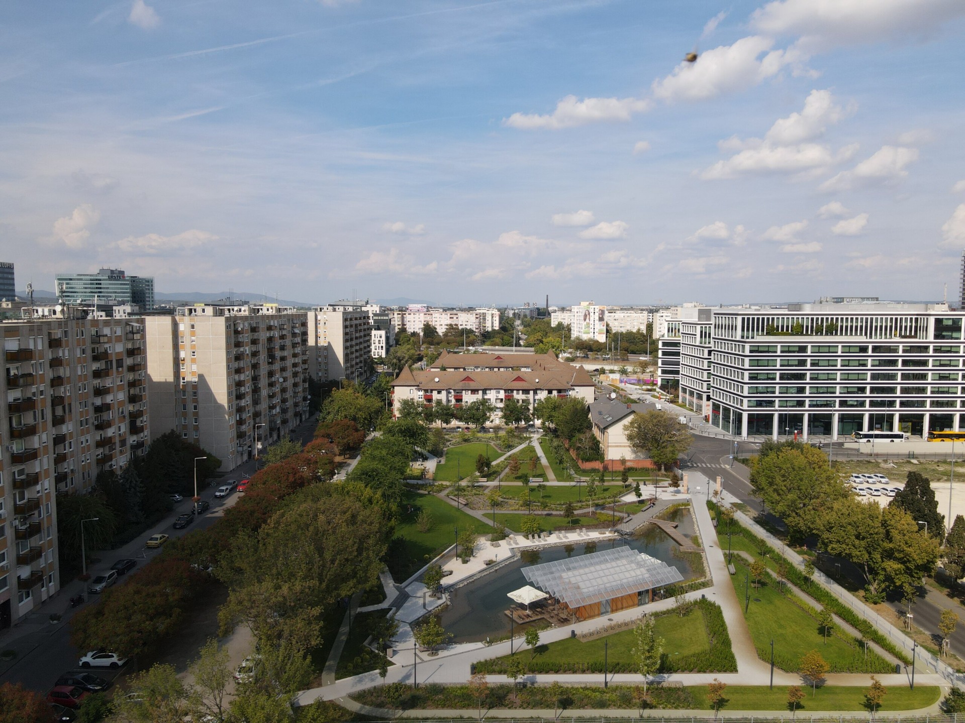 XIII. kerület városi panoráma lakóházakkal, parkos udvarral és modern irodaházakkal, kék égen gomolygó felhőkkel.